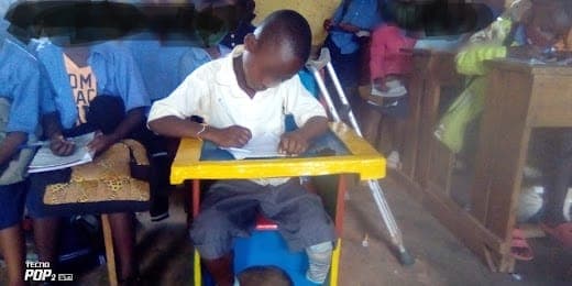 A young child sitting supported in a special chair, playing with building blocks on the tray